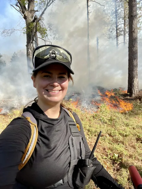 Woman smiling at the camera and standing in the forest.