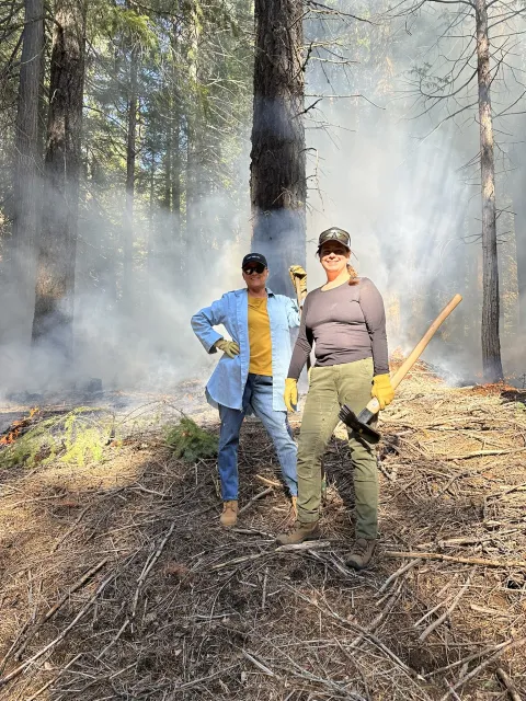 Two women standing in a forest during a prescribed burn.