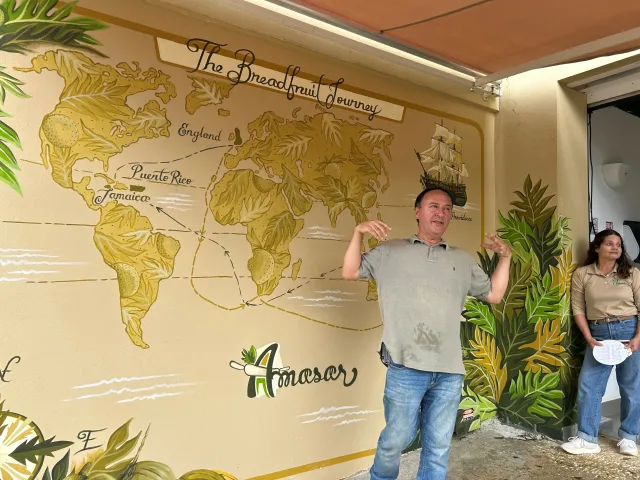 A man standing in front of a world map mural showing the breadfruit journey