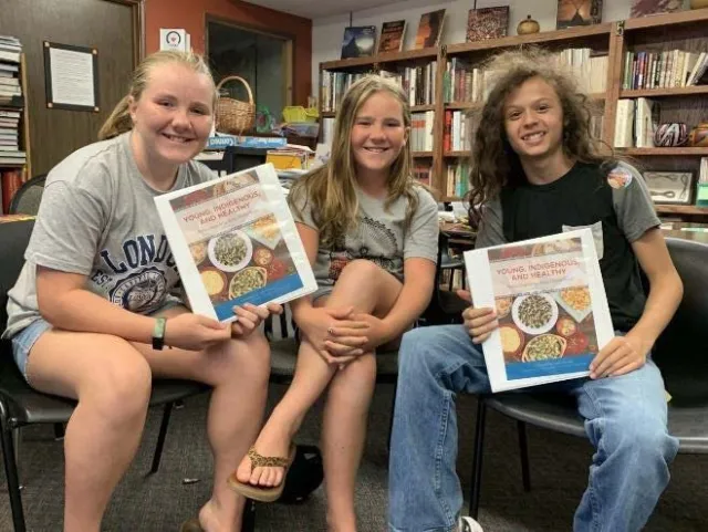 Young people at Foothill Indian Education Alliance facility pose with a cookbook of Native recipes
