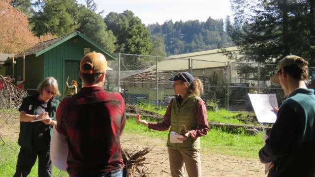 Woman standing in a circle of people leads a discussion.