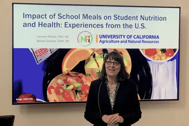 Nutrition researcher Lorrene Ritchie in front of a screen with her school meals presentation slide