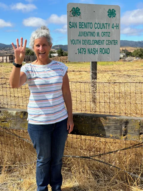 Freed raises four fingers in front of a 4-H Farm sign in San Benito County