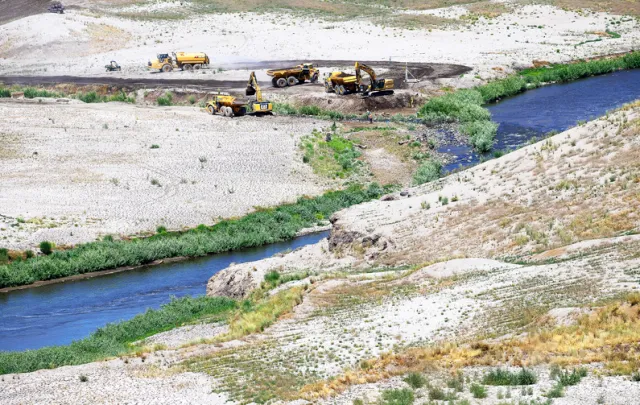 Yellow machinery moves silt next to the river
