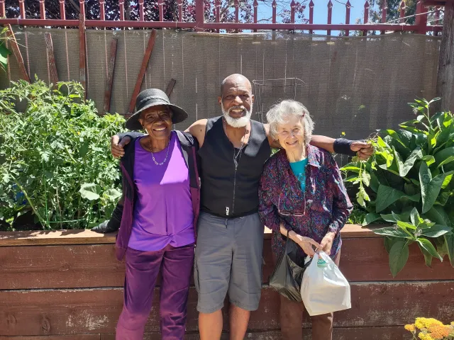 A man stands in the garden with his arms around women on his sides