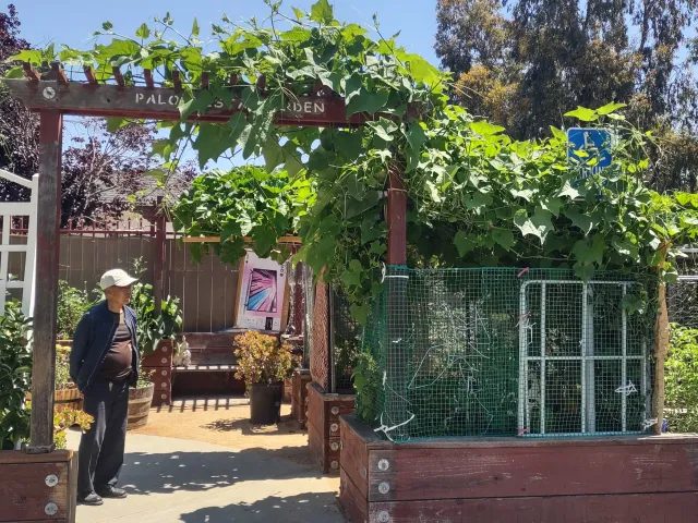 A person stands under the wood sign that reads, "Palo Vista Garden," that marks the garden entrance.