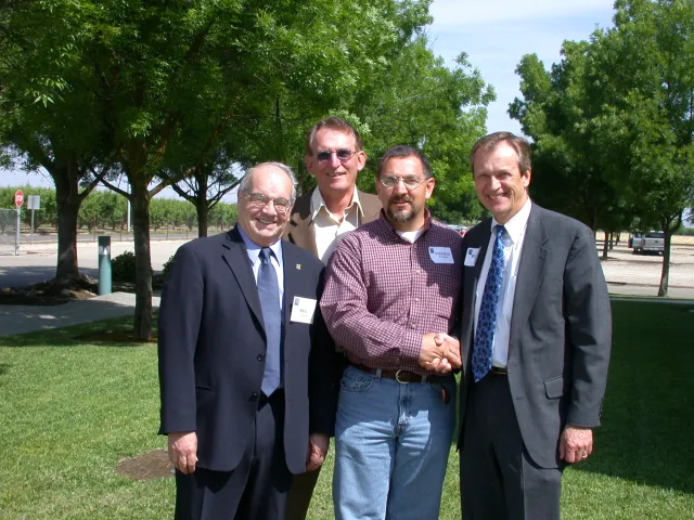 Four men standing on grass surrounded by trees