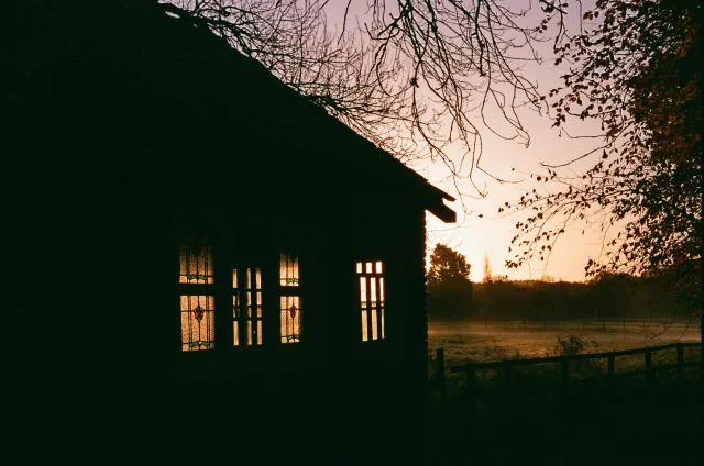The dark silhouette of a house with lit windows at dusk.