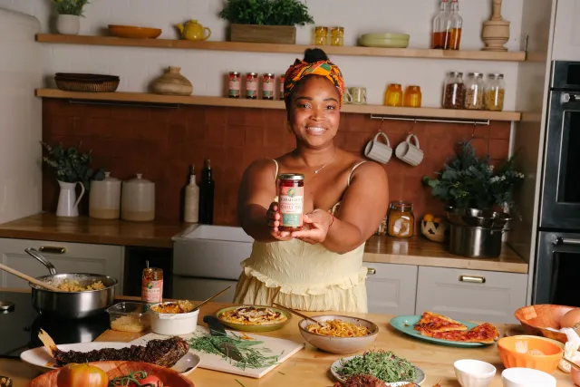 Gloria Allorbi stands in a kitchen holding a bottle of Ghanaian vegan chili oil