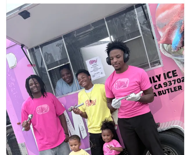 Paula peeks out the window of the pink Family Ice truck. Her 5 kids pose outside the truck