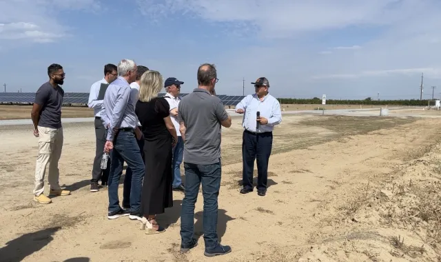 Group stands on edge of field with solar panels in background