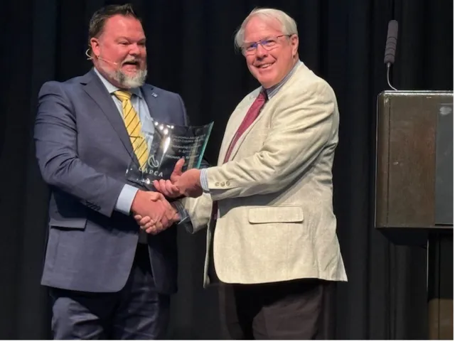 A man hands Michael Rethwisch an engraved lucite award while shaking his other hand.