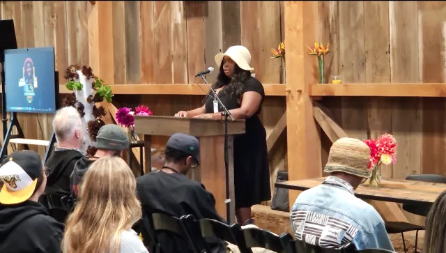 Sheyna Burns stands at a lectern to speak to audience