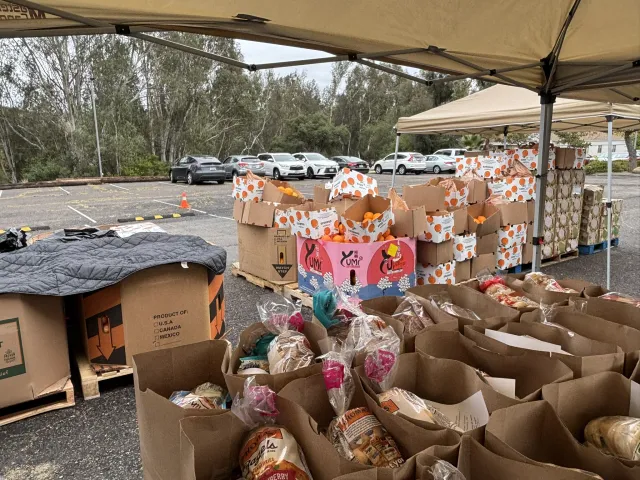 Bags of food sit on a table outside under a pop-up tent.