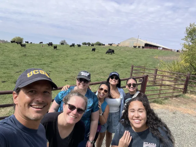 Seven people pose next to a pasture of grazing black cows