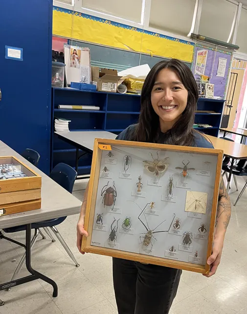 Mia holds glass case displaying bugs