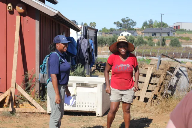Two women laugh as they stand next to a shed and pallets on a farm