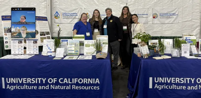 UC ANR staff stand at an exhibition table during EcoFarm 2026, showcasing materials related to various programs.