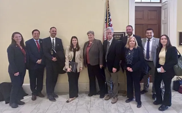 Ten people wearing business suits stand in front of U.S. flag
