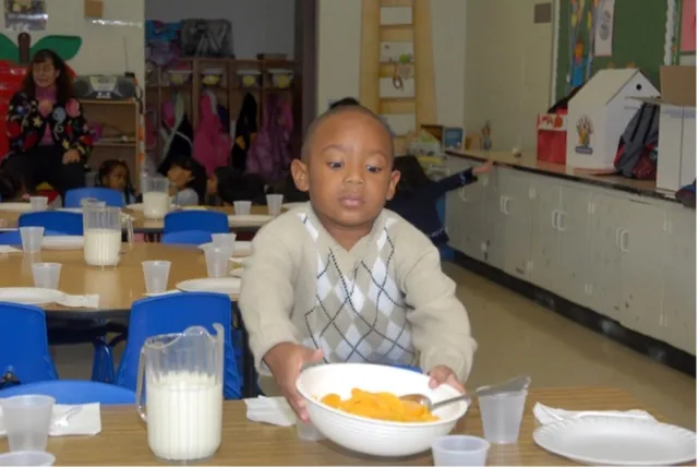 A young boy at a child care center grabs a bowl of canned fruit.