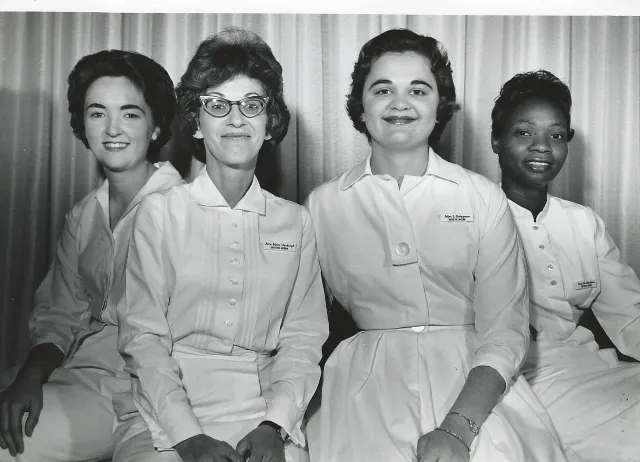 Three white women and one Black woman wearing white uniforms