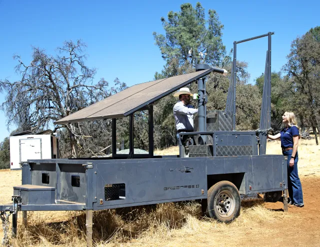 A man in a cowboy and woman in a blue polo confer over the maintenance of a GreenFeeder machine, which looks like a trailer
