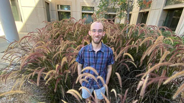 Justin stands outdoors among landscape plants