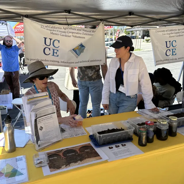 People around a table with UC Master Gardener materials on it and signs above.