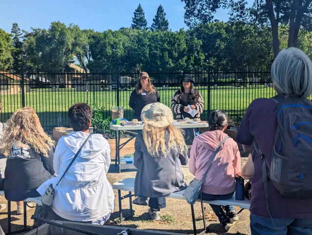 A group of five people seated in an outdoor garden listening to two UC Master Gardener volunteers present a gardening workshop on a sunny day.