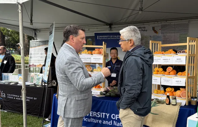 Grayson and Sandoval converse in front of ANR booth as Mike Hsu observes from the booth