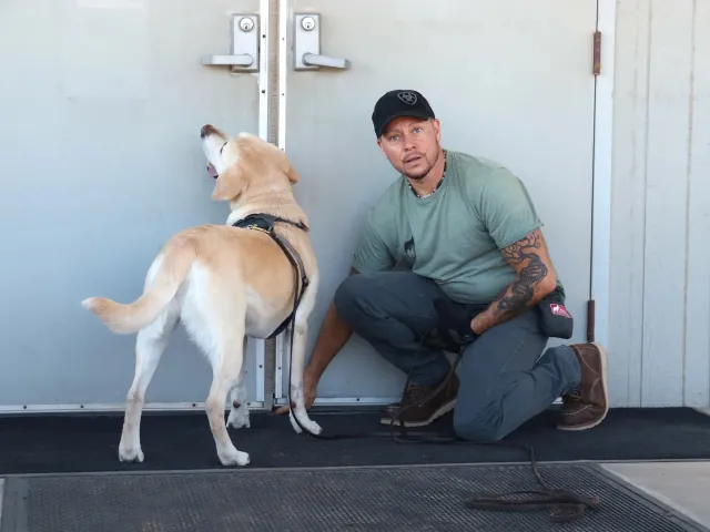 Man kneeling on ground next to a labrador dog.
