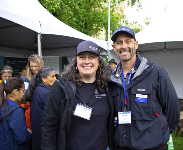 Sarah Light and Darren Haver pose standing in front of Missy Gable and other people at the Master Gardener Program booth
