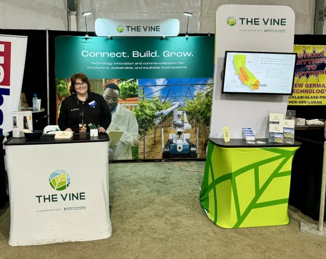 Terri stands smiling at the VINE booth. Banner behind her reads: Connect. Build. Grow.