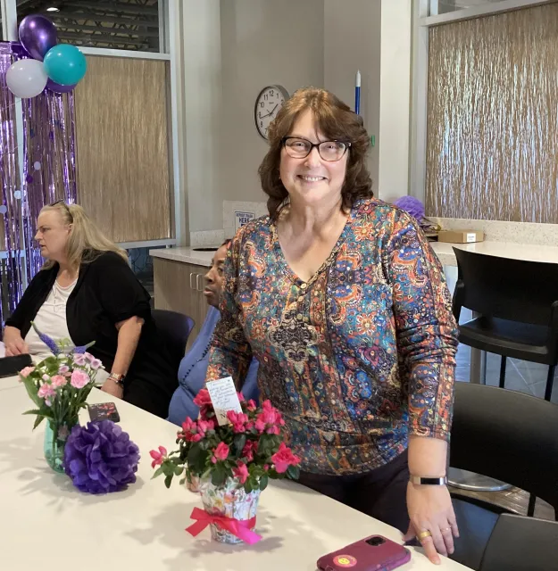 Terri poses next to flowers given to her at her retirement party. Jeri Hansen is in background