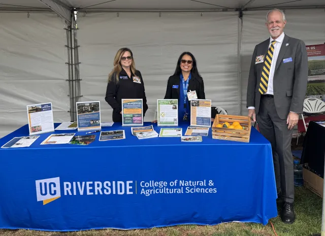 Two women and a man stand behind a table with a tabledrape that reads: UC Riverside College of Natural & Agricultural Sciences