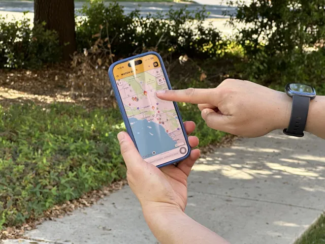 A disembodied hand points to an image of a flame on a map of California on a phone screen