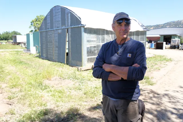 Tim Mueller stands with arms crossed as he gazes into the distance at his Riverdog Farm