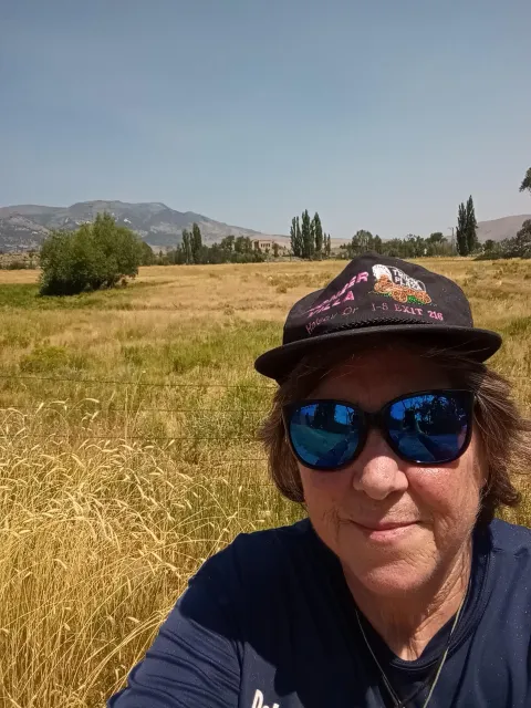 Laurie Wayne takes a selfie with the pasture of Locavore Farms behind her and mountains in the distance