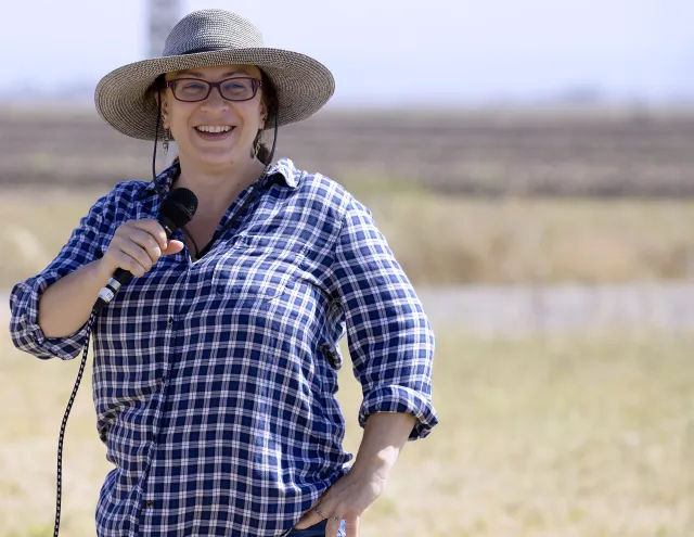 A person speaks into a microphone with a field in the background