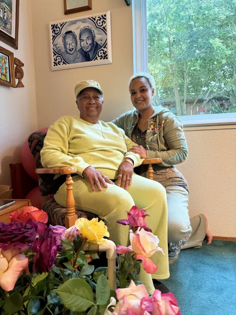 Iona and her granddaughter Jeanee posing by roses and a portrait of Iona and late husband.