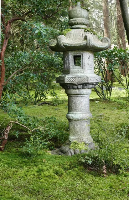 A beautiful Japanese lantern in a garden surrounded by moss and bushes.