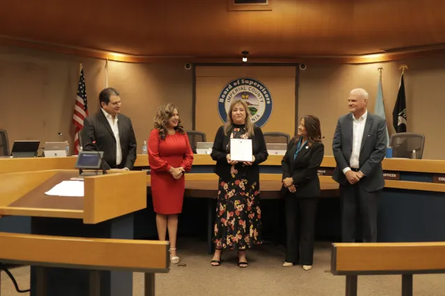 Martha S. Lopez holds a framed certificate as two people on either side of her look at her.