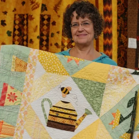 A HONEY BEE decorates a quilt at the 134th annual Dixon May Fair. Here Interior Living Showcase superintendent Debee Lamont gets ready to hang the quilt. It's the work of Shirley Geertson of Vacaville. (Photo by Kathy Keatley Garvey)