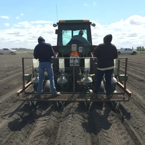Tractor pulling a research planter with two people operating the planter.