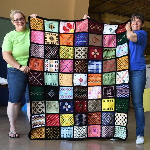 See the bumble bee on the aghan (top row)? This Minnesota sample afghan is the work of Debra Holter of San Pablo. Holding it are McCormack Hall superintendent Gloria Gonzalez (right) and assistant Kara Payne. (Photo by Kathy Keatley Garvey)