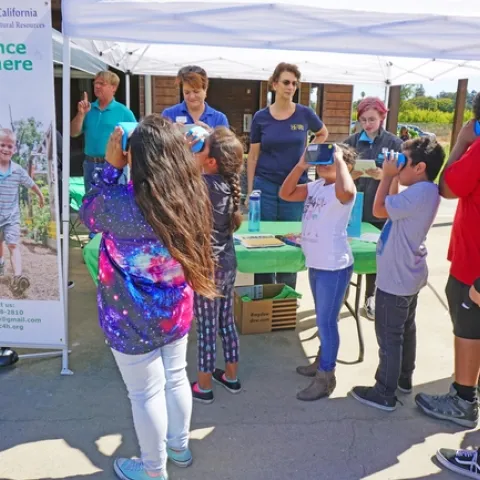 Children peer through VR goggles to see an undersea world, a 4-H activity shared with potential new members at the harvest festival. Behind the table from left are 4-H volunteer Stan Alger, 4-H program representative Sue Weaver, 4-H youth development advisor Fe Moncloa, and 4-H teen ambassador Alexa Russo.