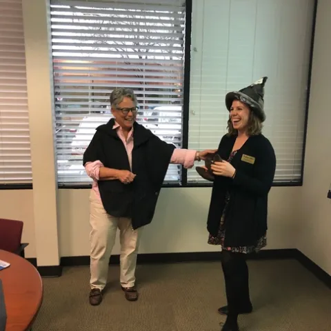 Two women, one touching arm of course instructor who is wearing a poop emoji hat.