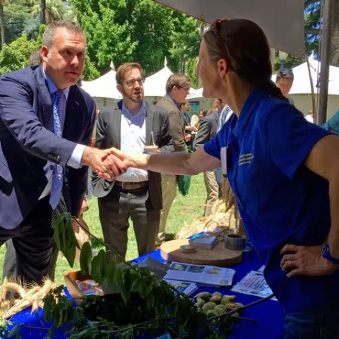 Assemblyman Gray, on left in navy-colored suit, shakes the hand of Michelle Leinfelder-Miles, who is wearing a blue ANR polo shirt.