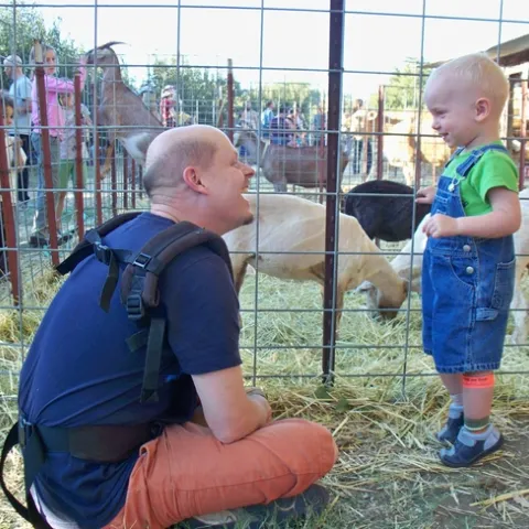Father and son enjoy a petting zoo on a farm offering agritourism experiences.
