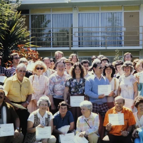 A group of freshly graduated UC Master Gardener volunteers in three rows holding up their certificates of completion.